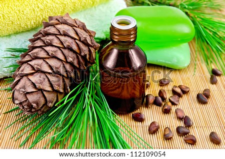 Cedar oil in a bottle, with a branch of cedar cones, cedar nuts, two green soap, two towels on a bamboo mat