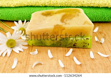 Homemade soap green and yellow, two towels, flowers and petals camomile against a wooden board