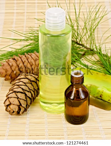 Cedar oil in a bottle, cedar cones with branch, two green homemade soap, shower gel on a bamboo mat