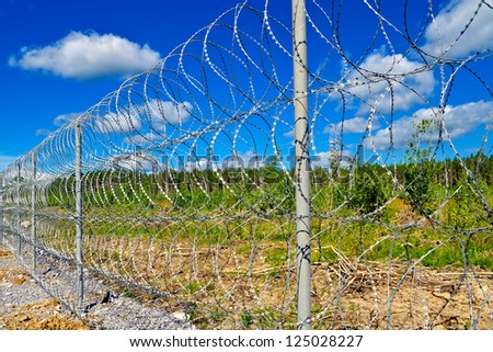 Barbed wire fence on a background of blue sky with white clouds, green trees