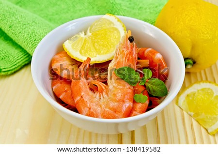 Raw shrimp in a white bowl with lemon, basil and green cloth on a wooden board