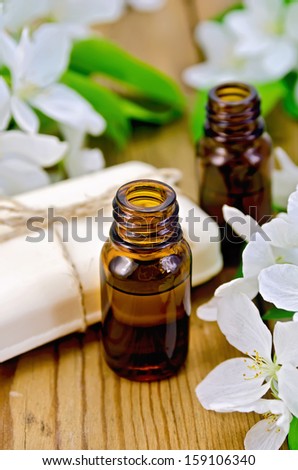 Two bottles of aromatic oils and white soap with flowers of apple on a wooden boards background