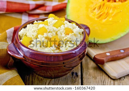Millet porridge with pumpkin in ceramic ware, raw pumpkin cut, knife, napkin on a wooden board