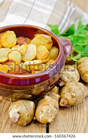 Jerusalem artichokes roasted in a clay pot, parsley, fresh artichoke tubers, napkin against a wooden board