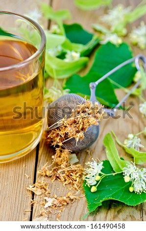 Metal sieve with dried flowers of lime, fresh flowers linden, tea in glass mug on a background of wooden boards