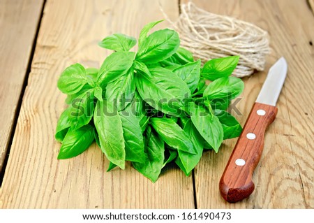A bunch of green basil with a skein of twine and a knife on a wooden boards background