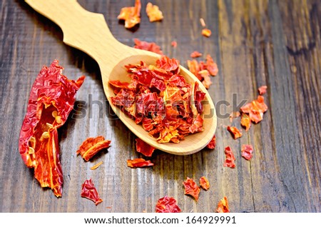 Red pepper flakes in a wooden spoon and a pod of dry red pepper on a wooden board