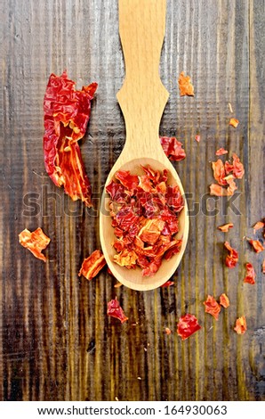 Red pepper flakes in a wooden spoon and a pod of dry red pepper on a wooden board on top