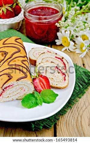 Biscuit roulade with cream and jam, a jar of jam, napkin, chamomile flowers, strawberries, mint on a wooden board