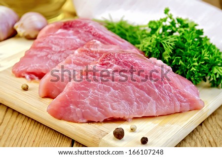 Three chunk of pork, garlic, parsley, dill, knife, pepper on a wooden boards background