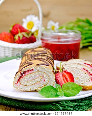 Biscuit roulade with cream and jam, jar of jam, napkin, chamomile, strawberries, mint on the background of wooden boards