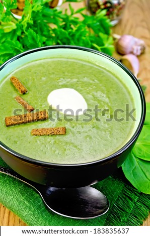 Green soup puree in bowl with a spoon on napkin, parsley, spinach, croutons, garlic and pepper on wooden board