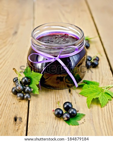 Black currant jam in a glass jar, fresh black currant berries with leaves on a wooden board