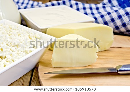 Suluguni, cottage cheese and sour cream in bowls, milk in glass jug, knife, napkin on the background of wooden boards
