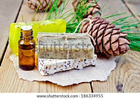 Cedar oil in a bottle, cedar cone, three homemade soap on a paper on the background of wooden boards
