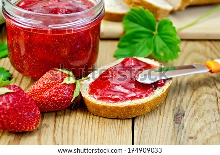 Bread with strawberry jam, a jar of jam, knife, strawberries on a wooden boards background