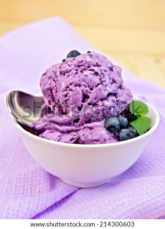 Blueberry ice cream with mint leaves in a bowl with berries, mint and spoon on a background of purple cloth and wooden boards
