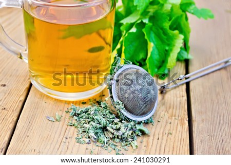Herbal tea in a glass mug, metal sieve with dry mint leaves, fresh mint leaves on a wooden boards background