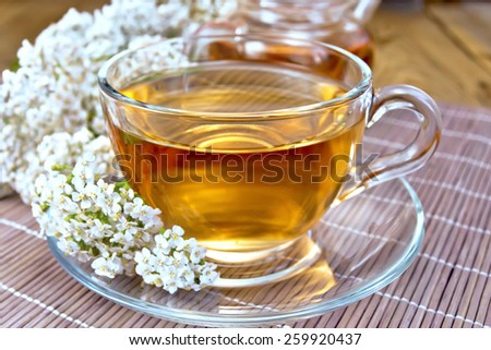Yarrow tea in a glass cup and teapot, fresh yarrow flowers on a background of bamboo boards and salfeki