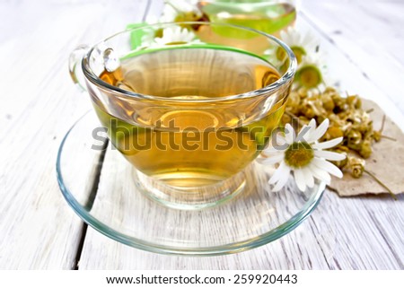 Tea in a glass cup, dry chamomile flowers on paper, fresh daisy flowers on a background of light wooden boards