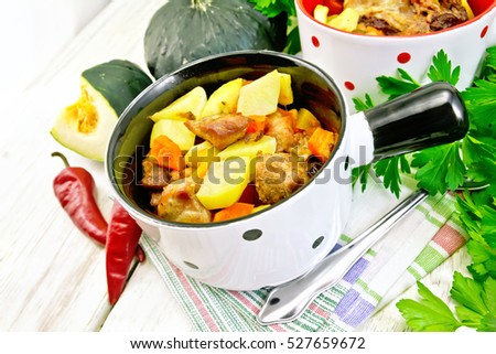 Roast with chicken, potatoes, squash and peppers in two portioned white pot on a towel, spoon, parsley on a wooden boards background