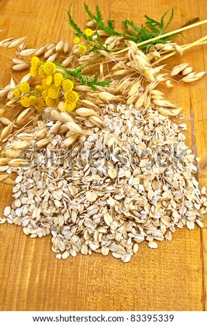 Oat flakes with yellow wildflowers the tansy and stalks of oats on a wooden board