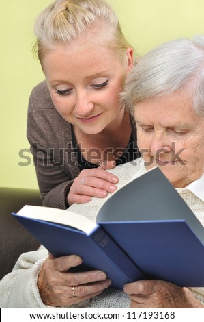 Senior woman with her caregiver in home reading book. MANY OTHER PHOTOS WITH THIS SENIOR MODEL IN MY PORTFOLIO.