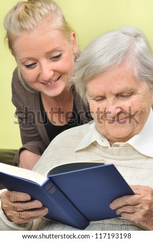 Senior woman with her caregiver in home reading book. MANY OTHER PHOTOS WITH THIS SENIOR MODEL IN MY PORTFOLIO.