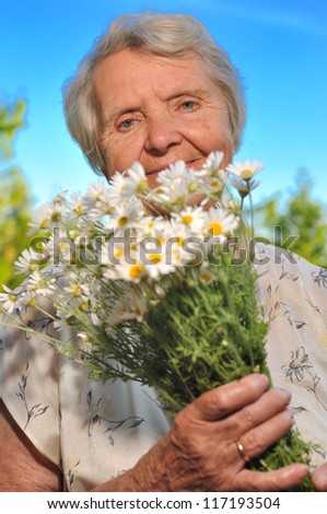 Senior woman smelling flowers on blue sky. MANY OTHER PHOTOS WITH THIS SENIOR MODEL IN MY PORTFOLIO.