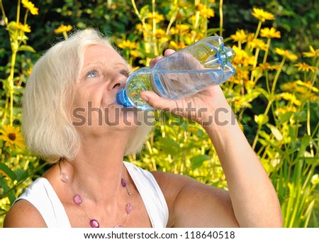 Mature, blonde woman drinking water from bottle in garden.