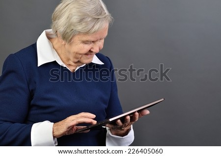 Senior happy woman with tablet against grey background.