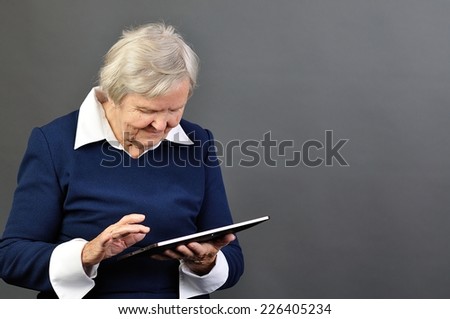 Senior happy woman with tablet against grey background.