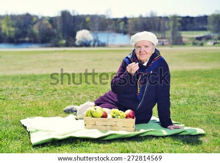 Senior happy woman sitting on a blanket on glade in the park. Healthy outdoor activities. Happy and smiling. MANY OTHER PHOTOS FROM THIS SERIES IN MY PORTFOLIO.