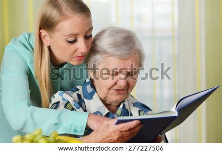 Senior woman with her caregiver in home reading book. MANY OTHER PHOTOS FROM THIS SERIES IN MY PORTFOLIO.