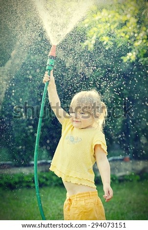 Little girl playing in the garden pouring all the water from a garden hose. MANY OTHER PHOTOS FROM THIS SERIES IN MY PORTFOLIO.