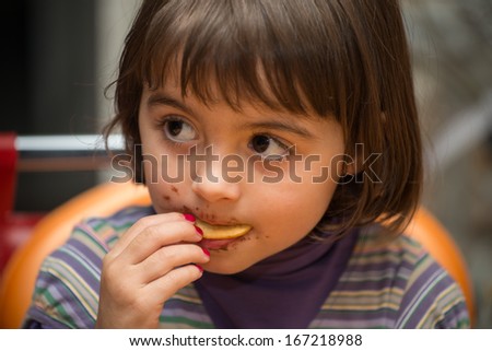 Baby girl with dirty face eating chocolate cake.