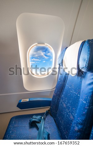 Airplane seat and window inside an aircraft with view on clouds.