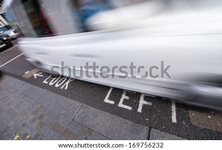 Look Left warning at a pedestrian crossing in a London street with car speeding up.