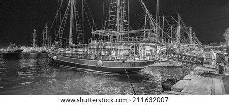 KOS, GREECE - JUNE 7, 2014: Typical wooden daily boats trip in the port of Kos Town at night. The Bar Street behind the boats, nightlife center of touristic town.