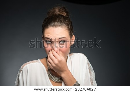 Portrait of a young woman holding her nose because of a bad smell. Isolated against gray background.