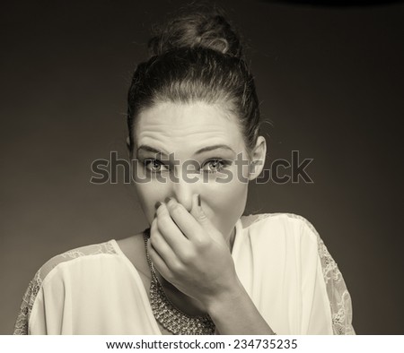 Portrait of a young woman holding her nose because of a bad smell. Isolated against gray background.
