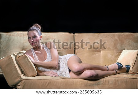 Green eyed brunette woman laying on the sofa with sensual behaviour. Isolated on black.