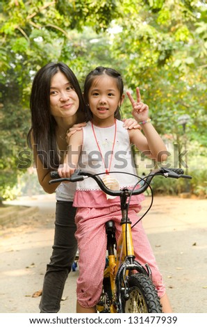 chinese mother having good time on bicycle with her daughter outdoor, peace sign