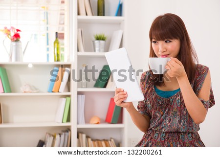 Portrait of smiling chinese woman using laptop with livingroom background drinking coffee