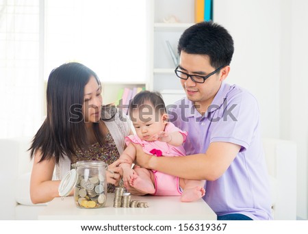 Asian baby putting coins into the glass bottle with help of parents. Money saving education concept.
