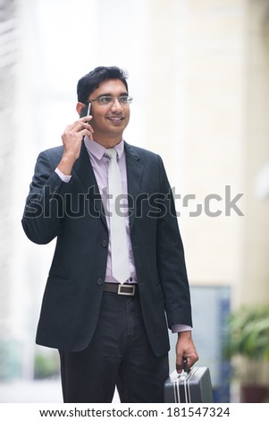asian indian business male on a phone with suit case