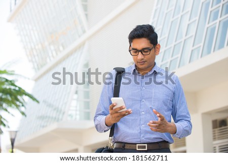 confused looking indian business male on a smartphone with office background