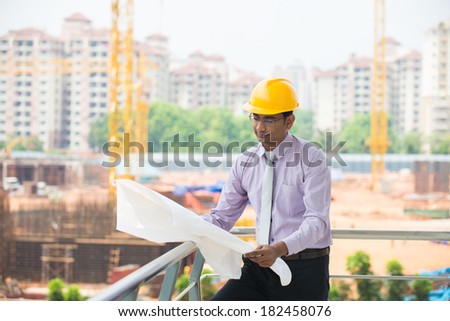 indian male architect reading plans with construction background