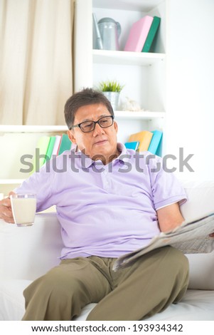 senior asian chinese  reading newspaper on a sofa in home