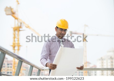 indian male engineer reading plans with construction background